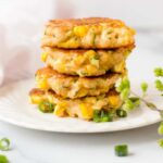 Zucchini and corn fritters stacked on a plate and garnished with green onions