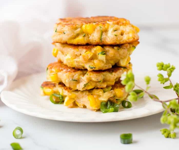 Zucchini and corn fritters stacked on a plate and garnished with green onions